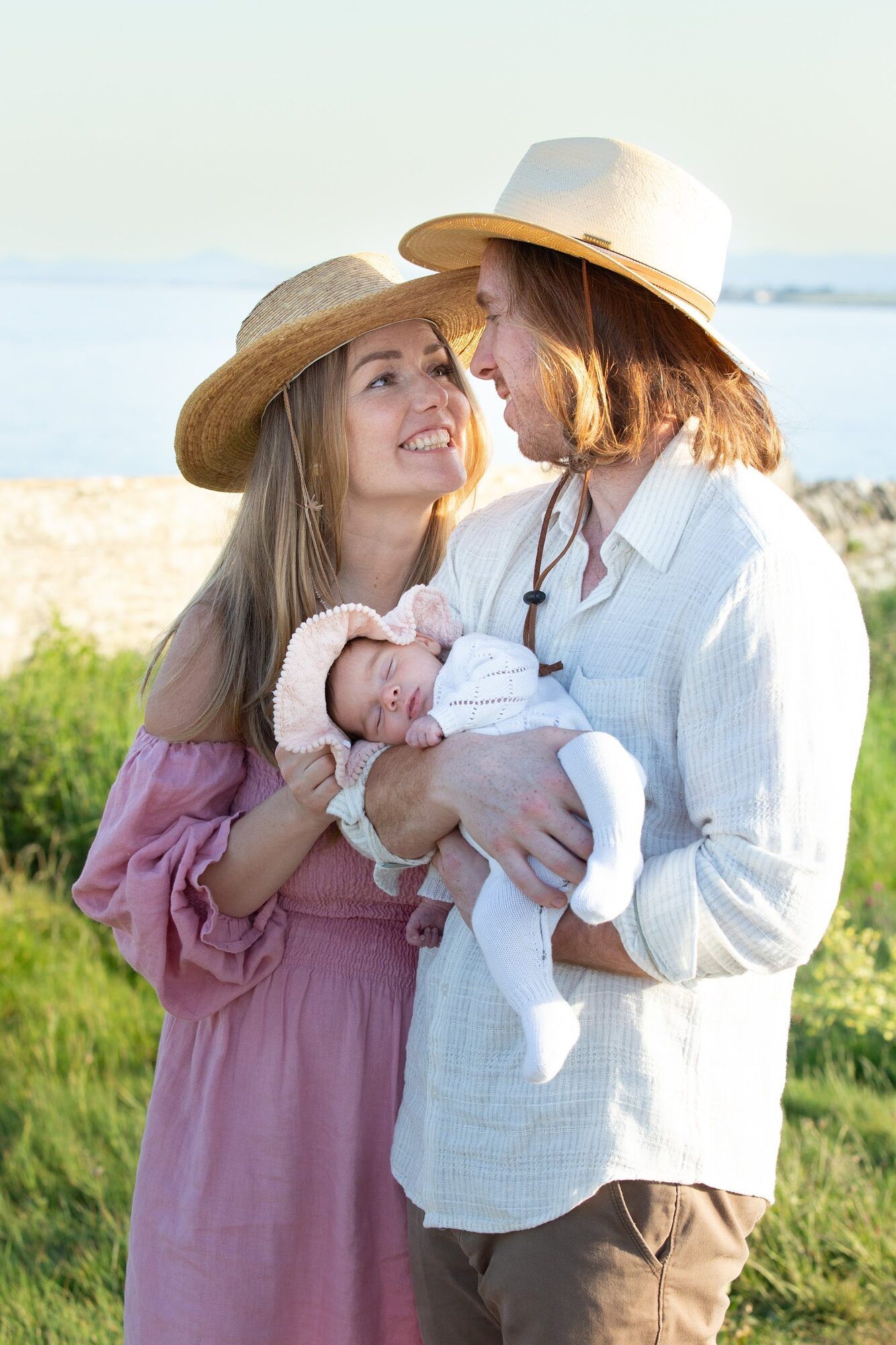 Parents in straw hats holding their newborn by the sea