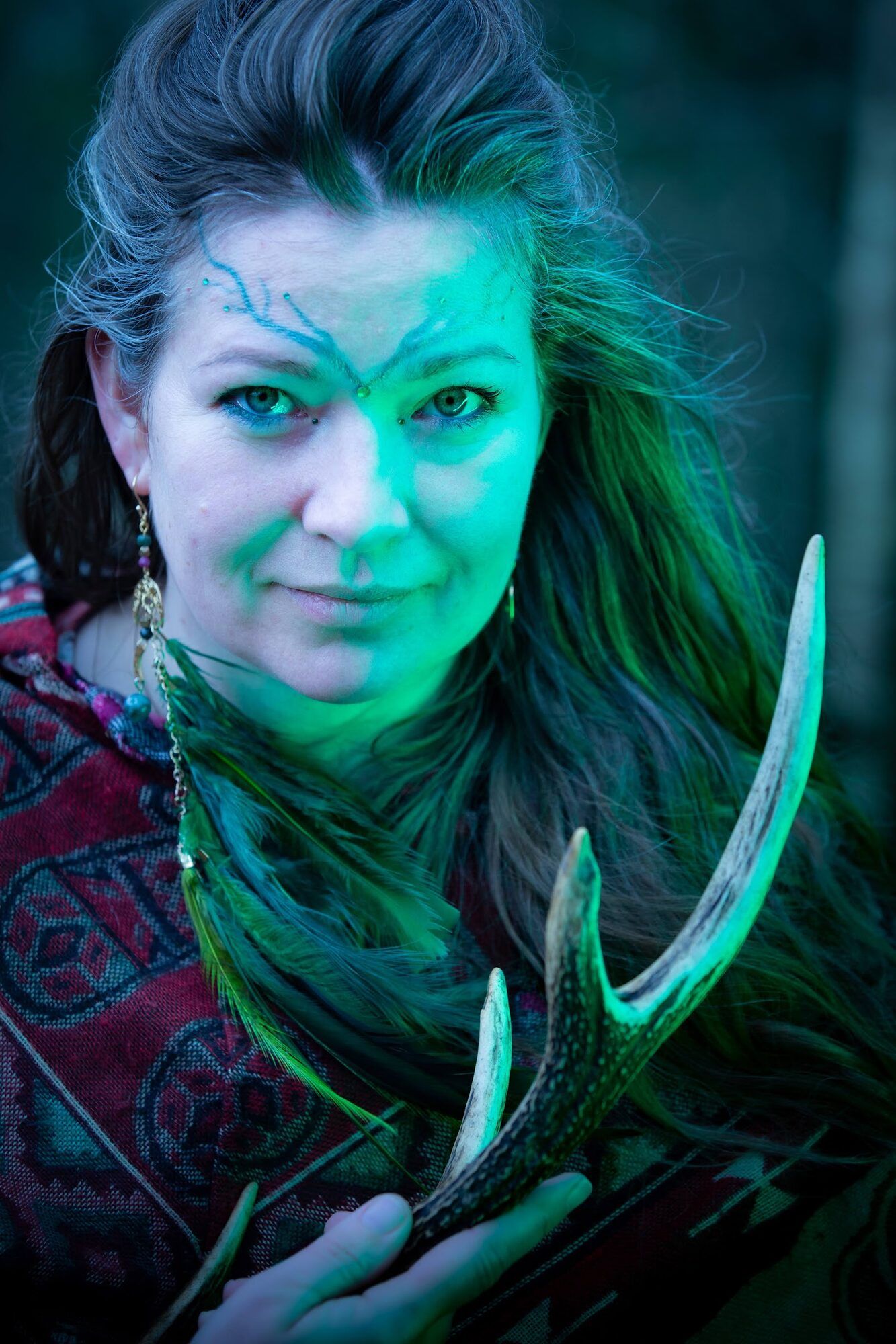 Woman with blue face paint holding an antler, green and blue light