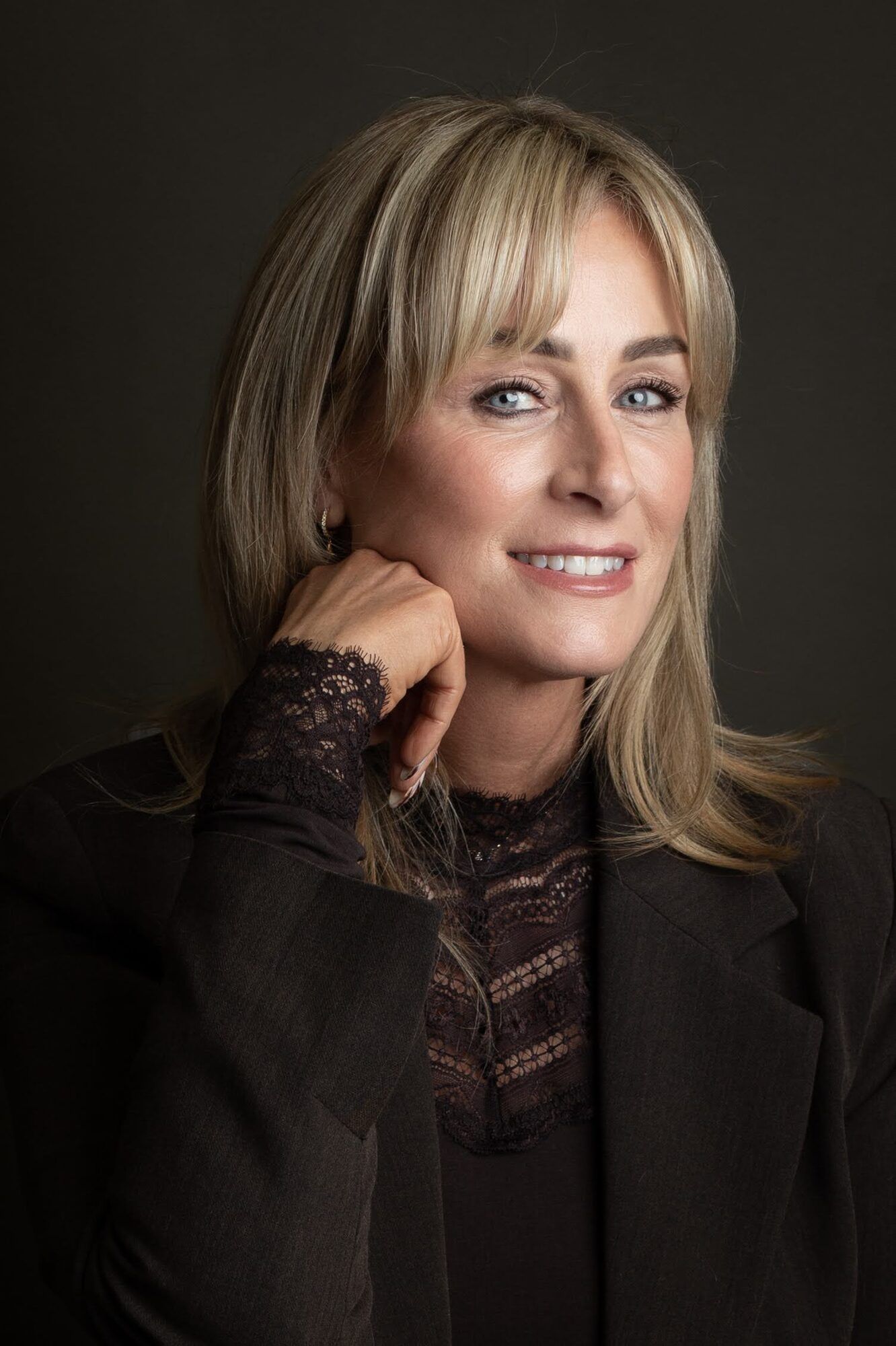 Blonde woman with a fringe, hand at her cheek, dark backdrop