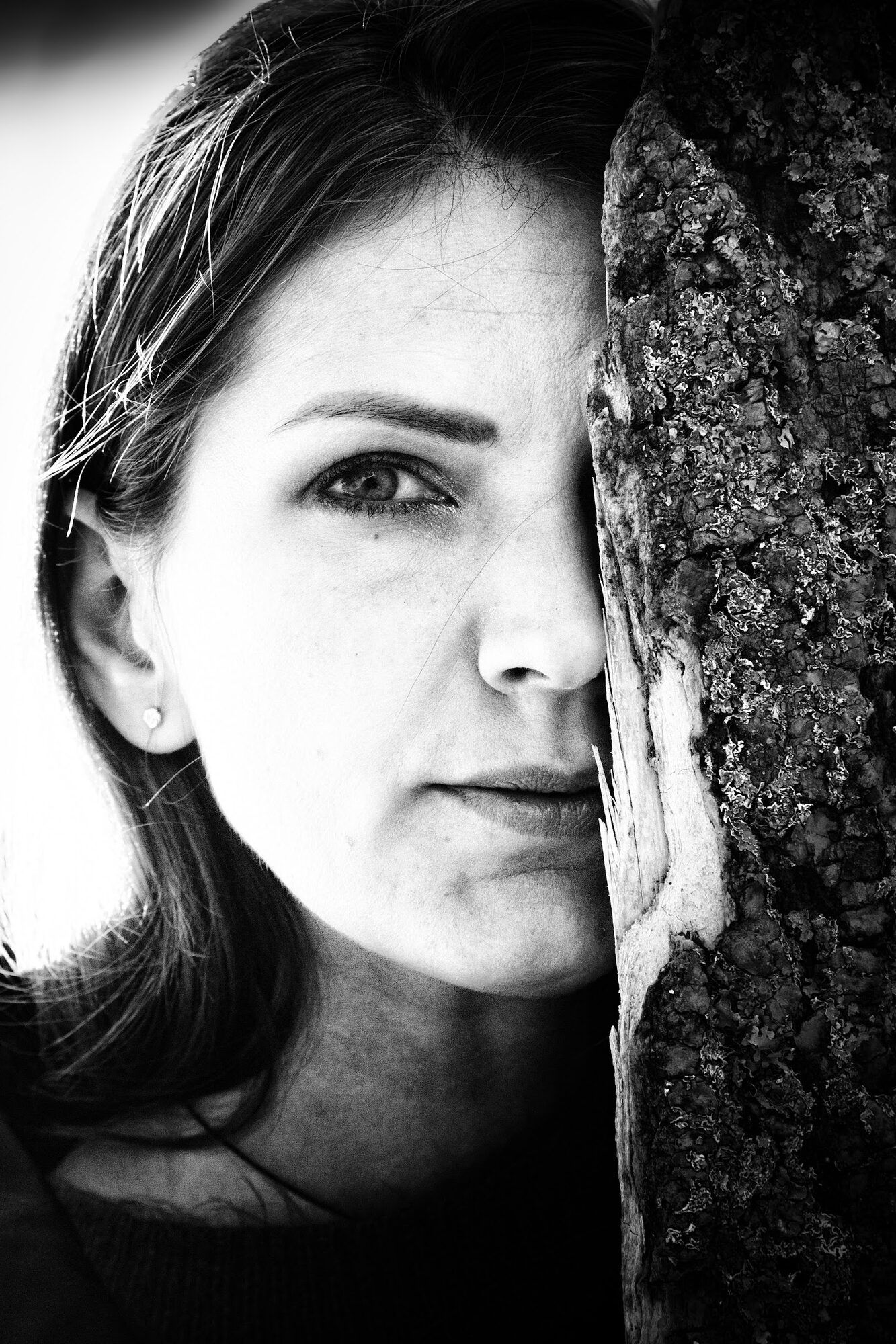 Black and white: half a woman’s face beside a tree trunk