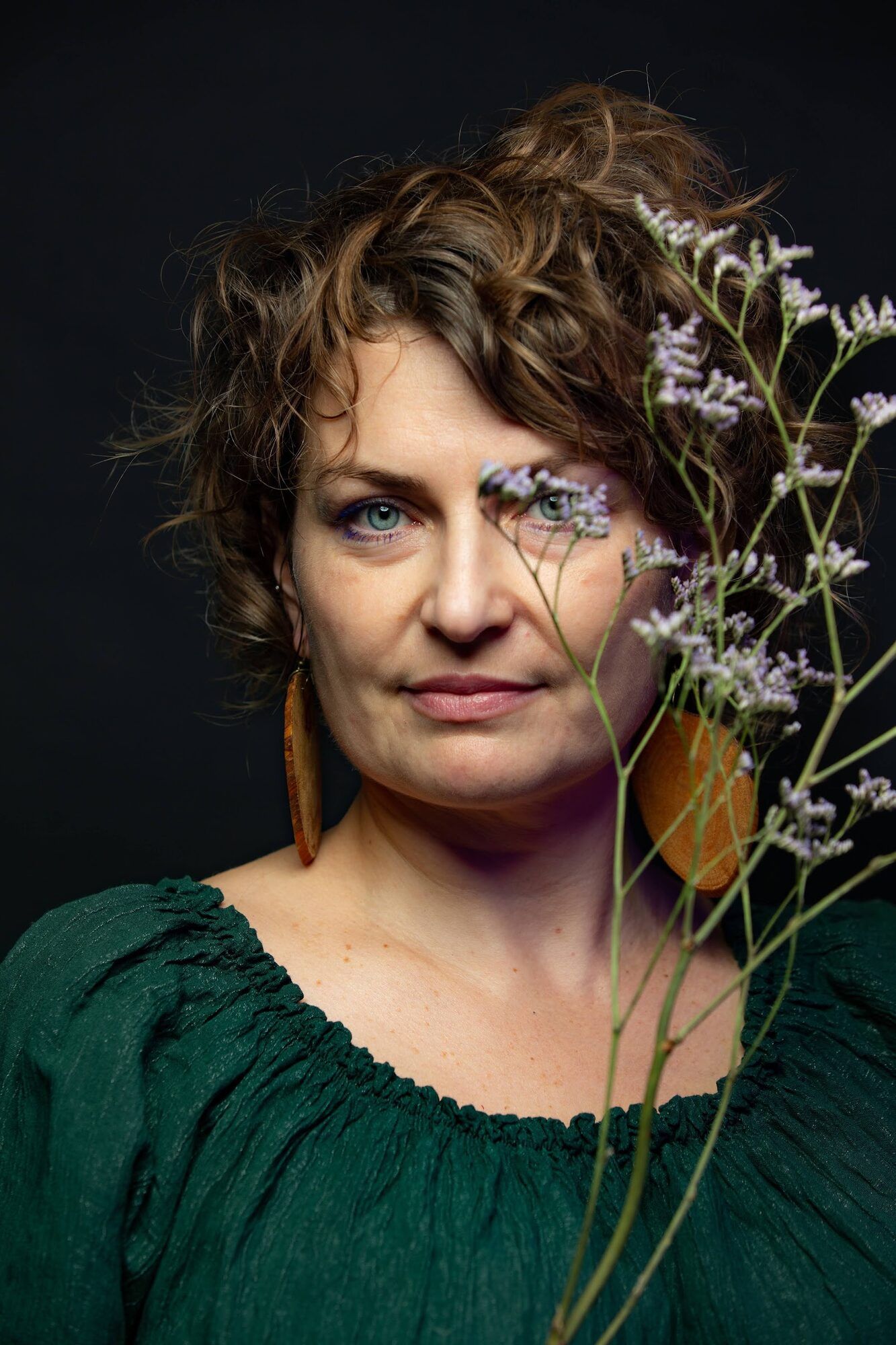 Woman with curly hair holding dried flowers in front of one eye
