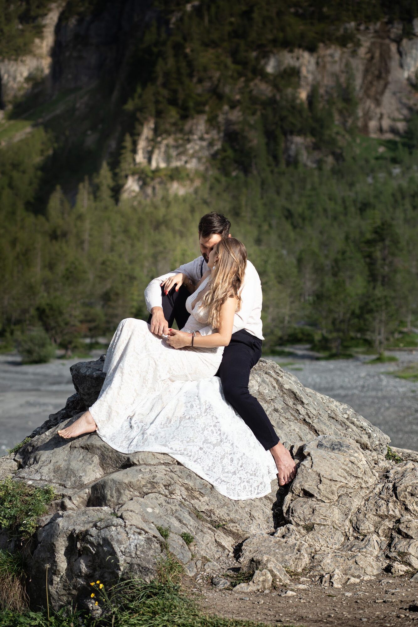 Couple sitting close on the rocks, lace dress spread around