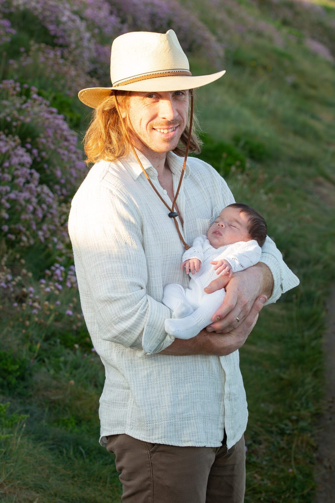 Father in a straw hat holding the baby among sea pinks