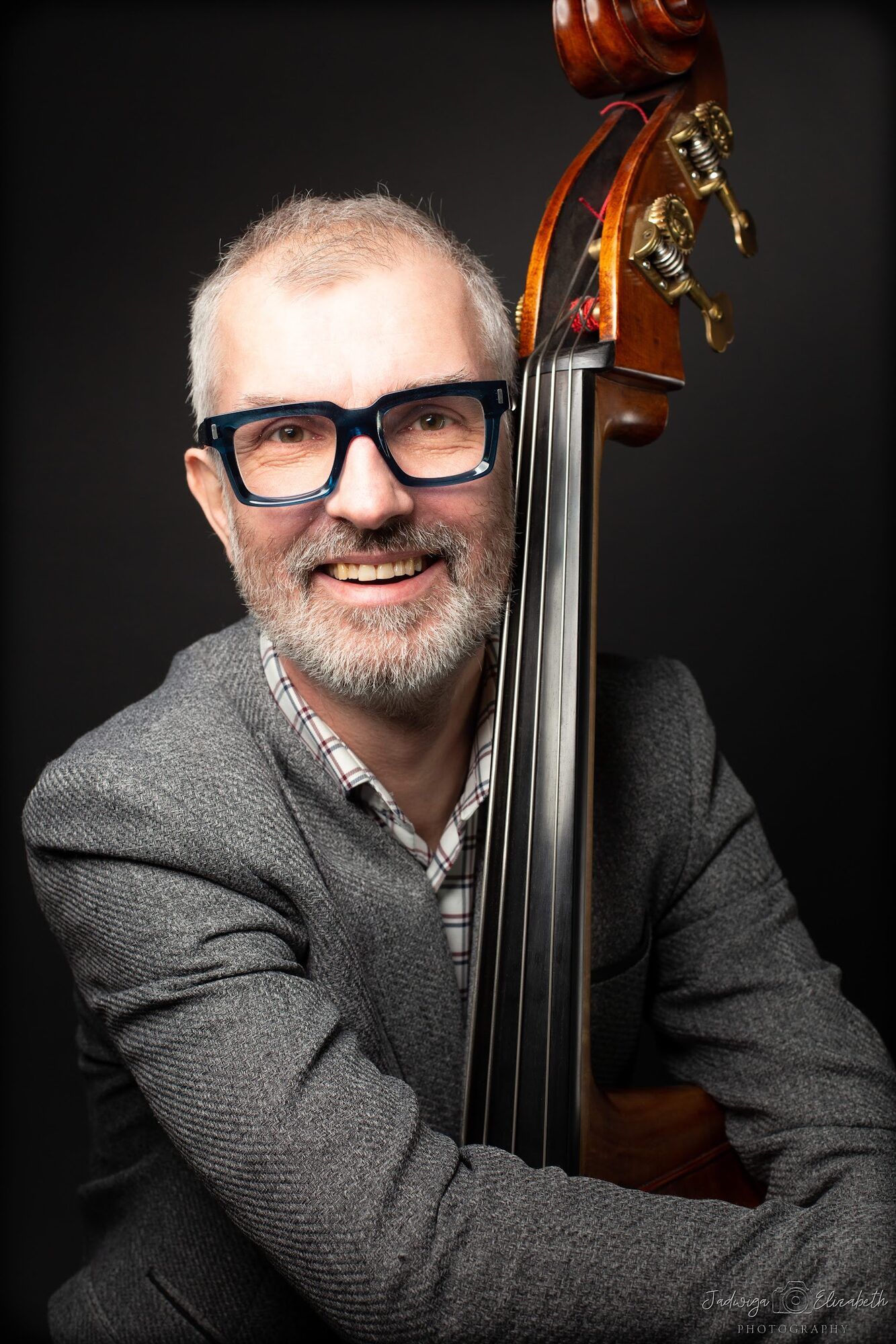 Smiling man in black glasses leaning on a double bass