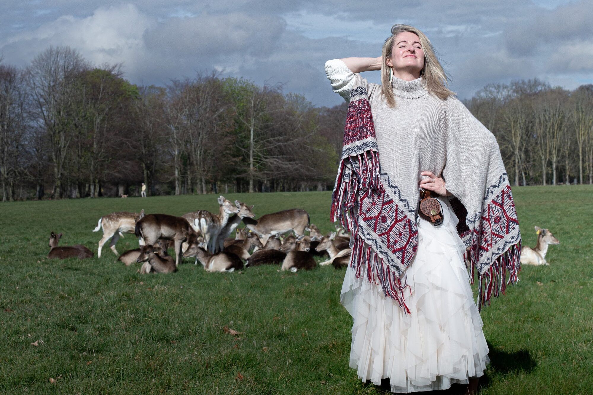 Woman in a woven poncho with reindeer grazing behind