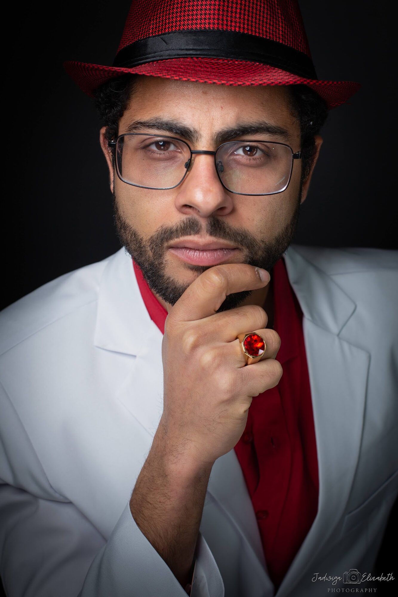 Man in a red hat and white suit, hand at his chin