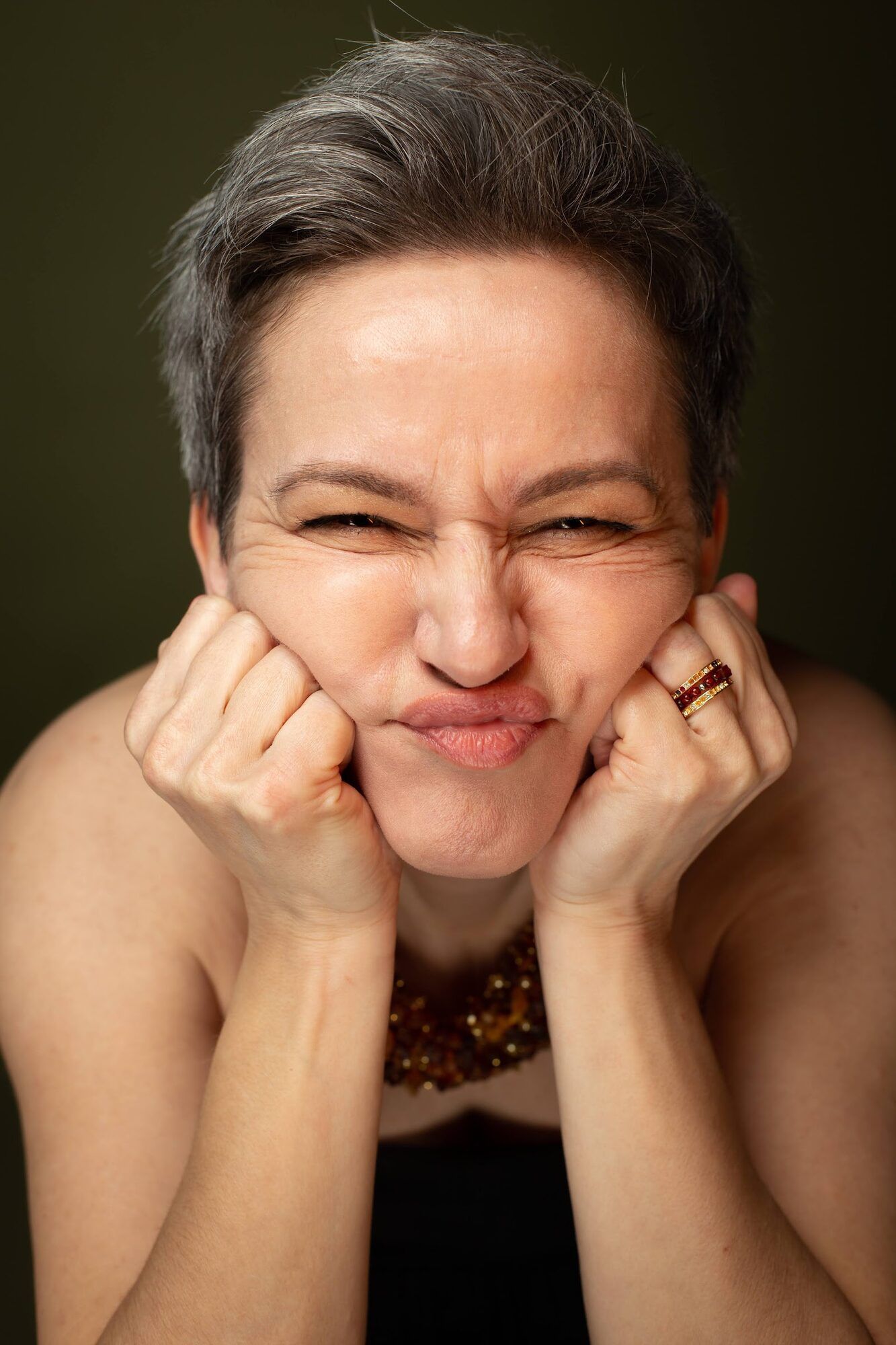 Woman with short grey hair pulling a face, hands on her cheeks