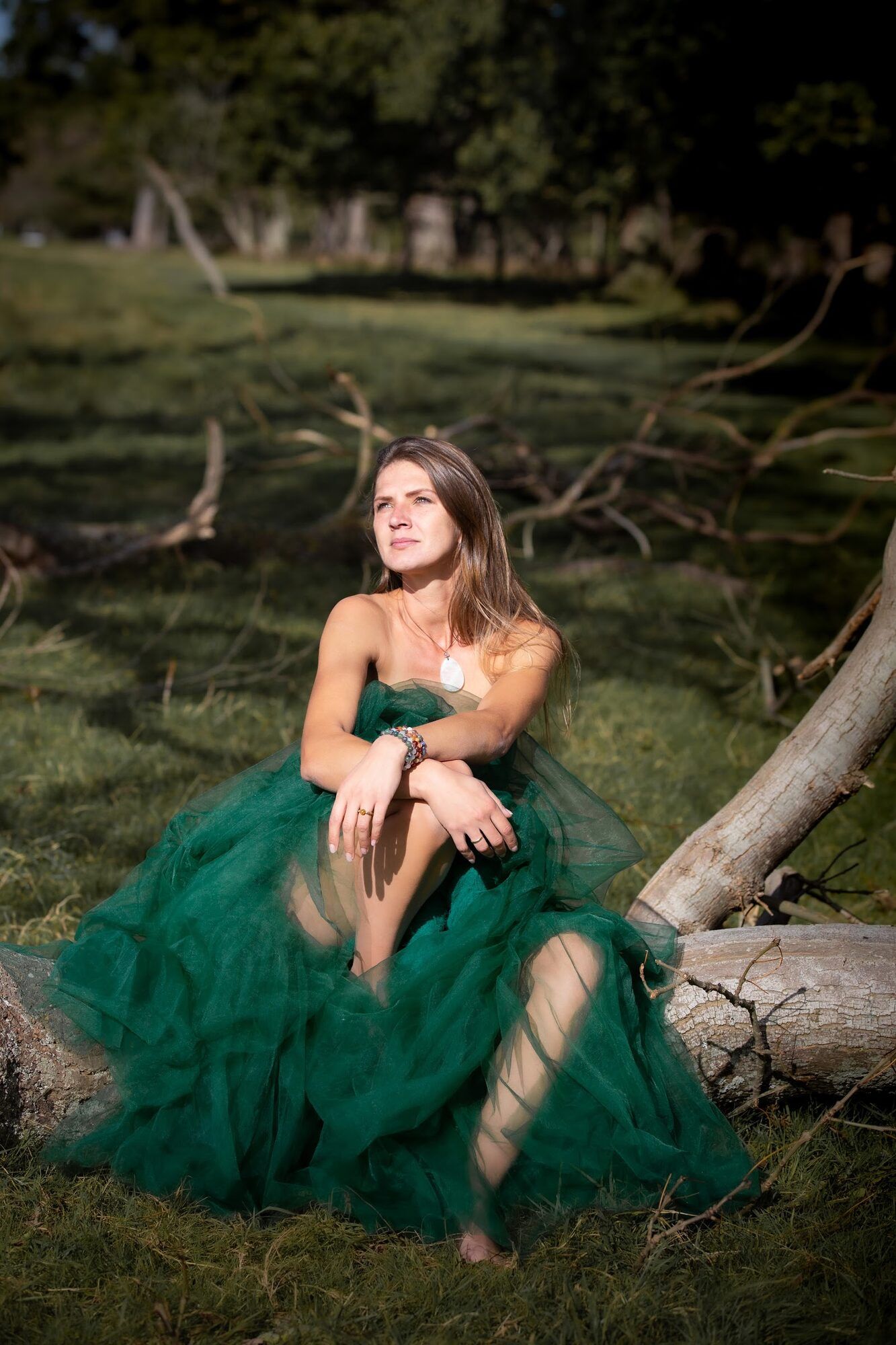 Woman in a green gown sitting on a fallen tree