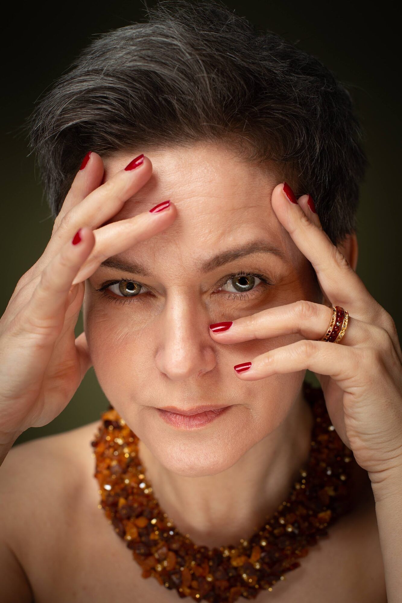 The same woman framing her face with her hands, amber necklace
