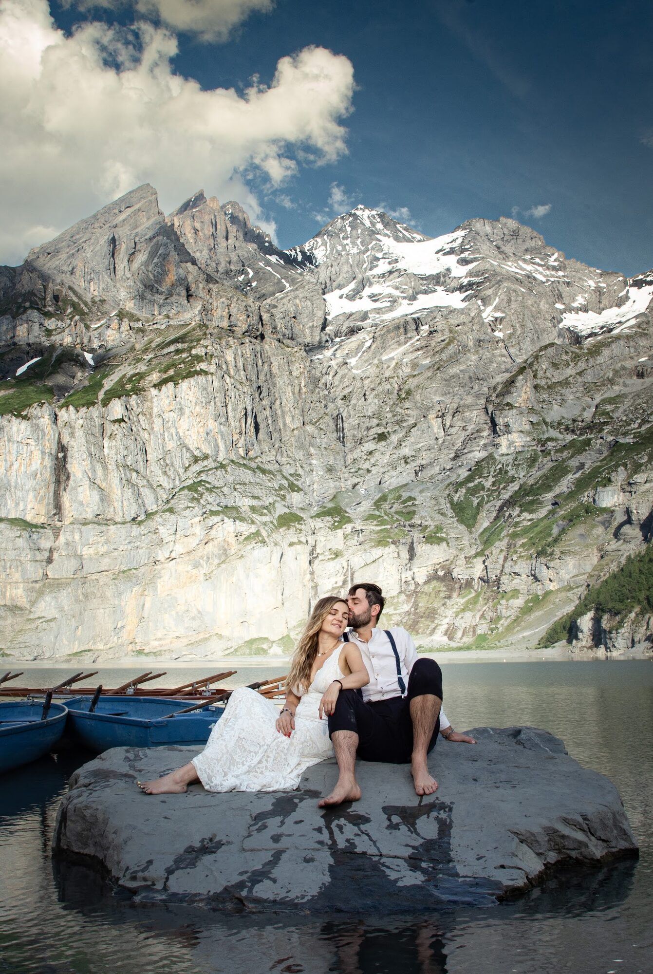 Couple on a flat rock in the lake, rowing boats behind