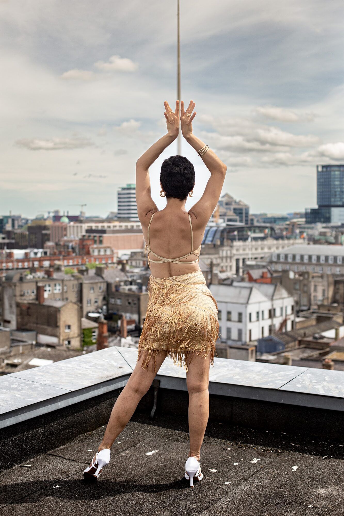Dancer in gold fringe, arms raised over the city