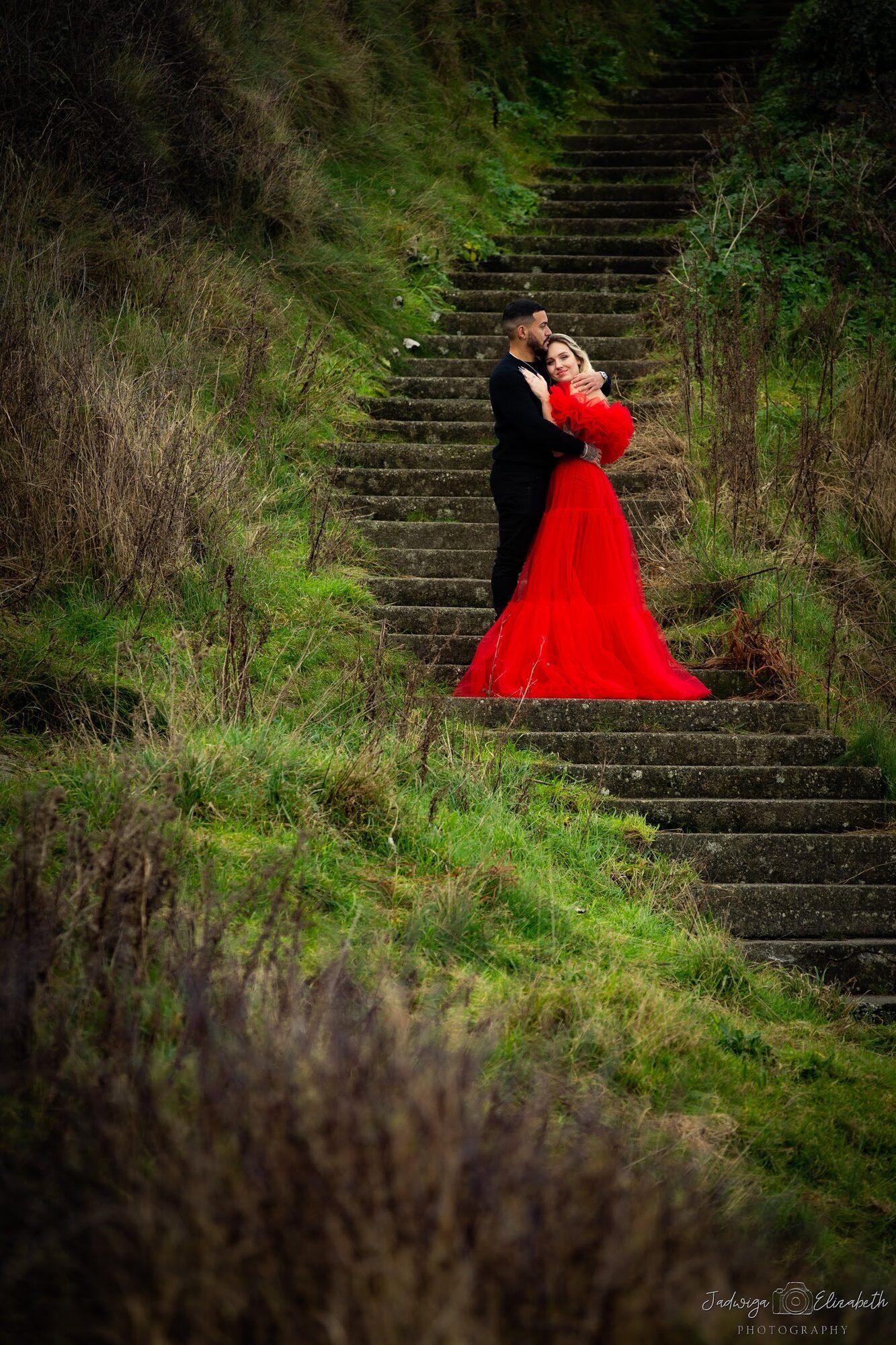Couple on mossy stone steps, she in a red gown