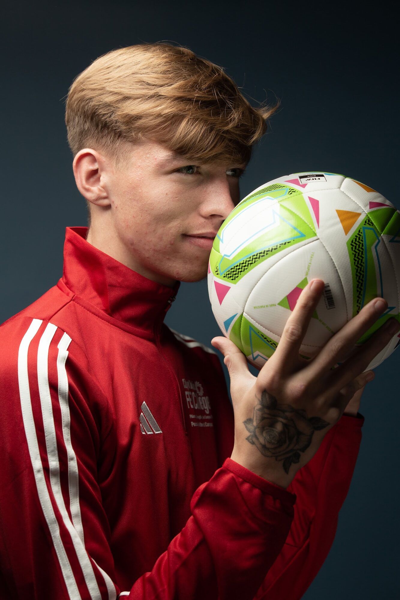 Young man in a red tracksuit top holding a football to his cheek