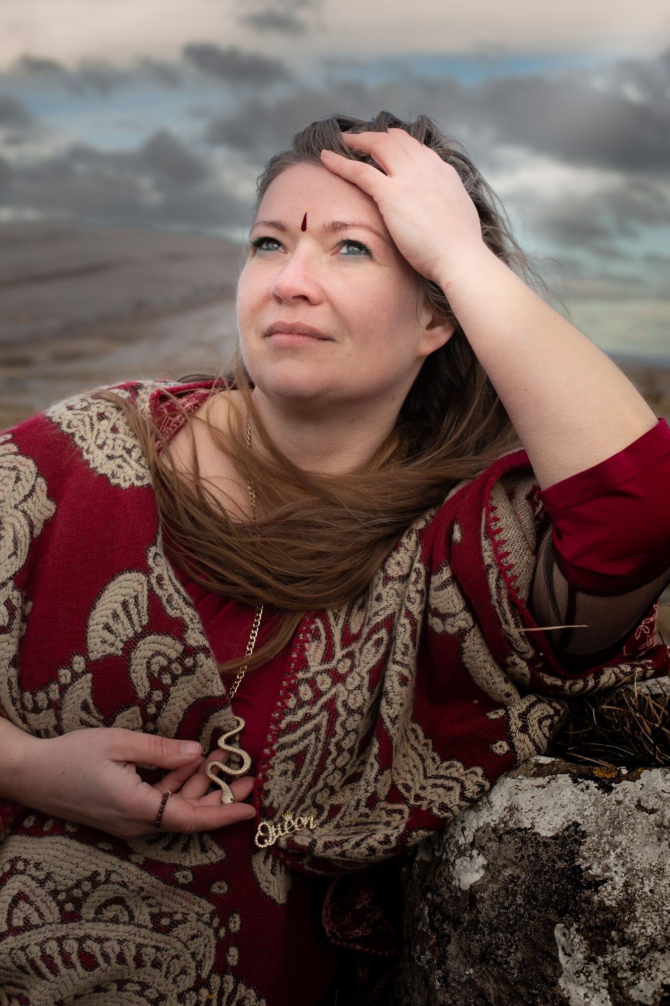 Woman in a red patterned dress by the sea, hand on her forehead