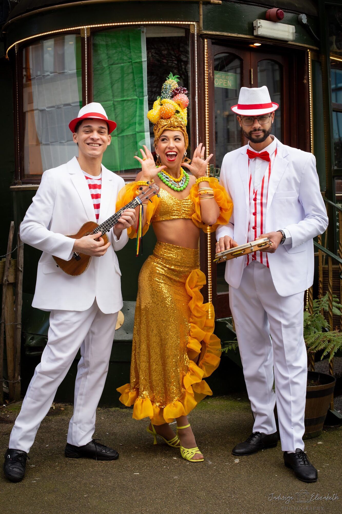 Two musicians in white with a dancer beside an old tram