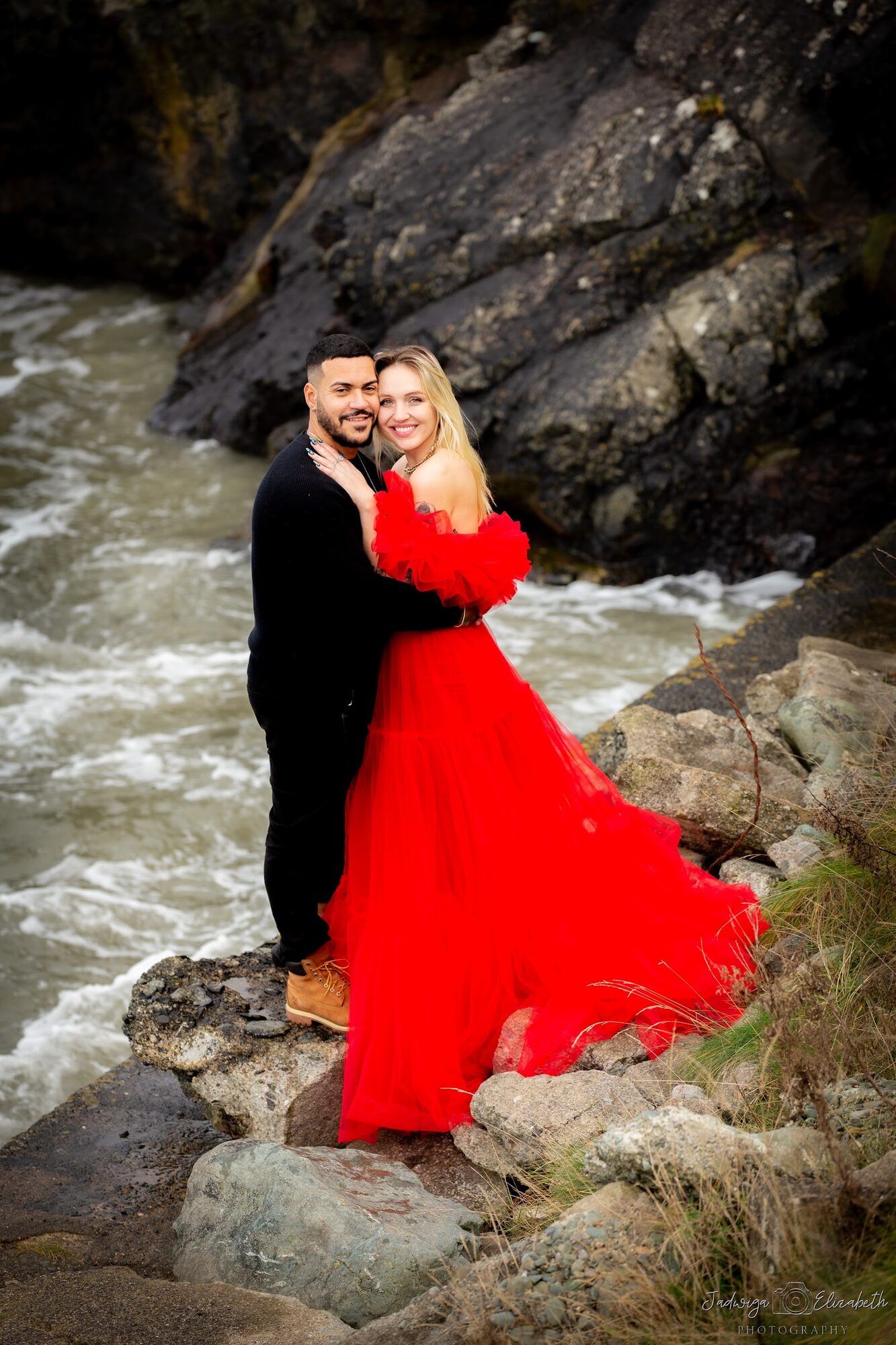 Couple on the rocks above the waves, red tulle gown