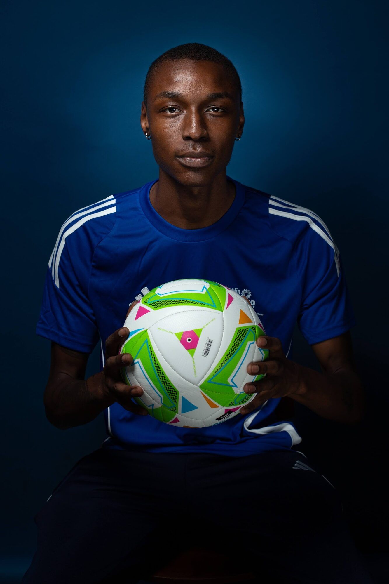 Young footballer in a blue shirt holding a ball, dark blue backdrop