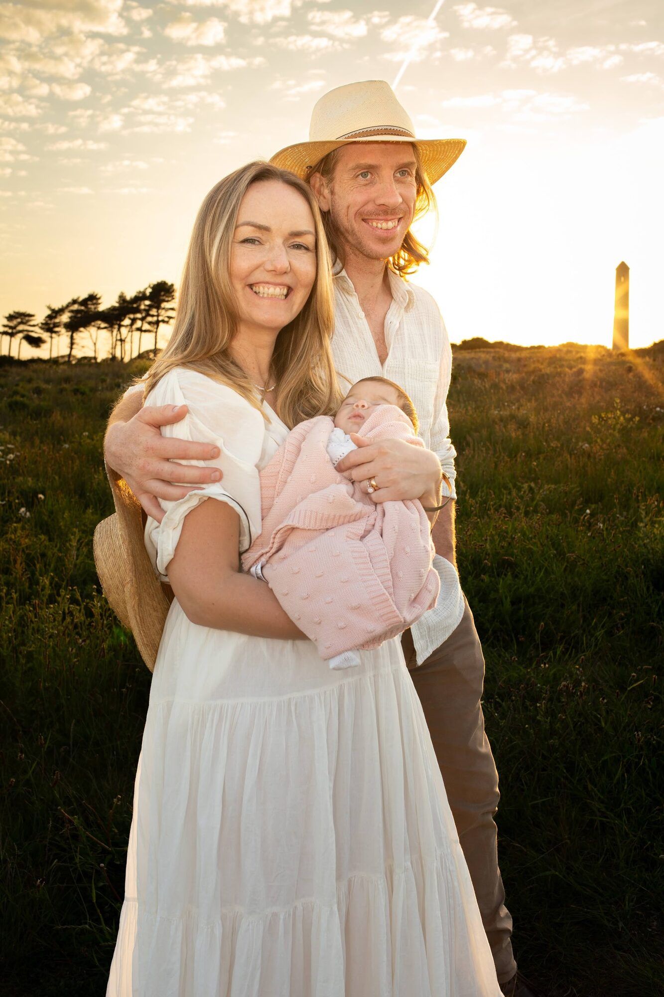 Parents with the baby at sunset, a lighthouse behind