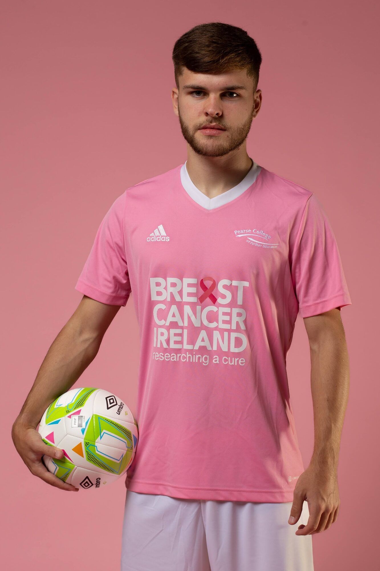 Young man in a pink football shirt holding a ball, pink backdrop