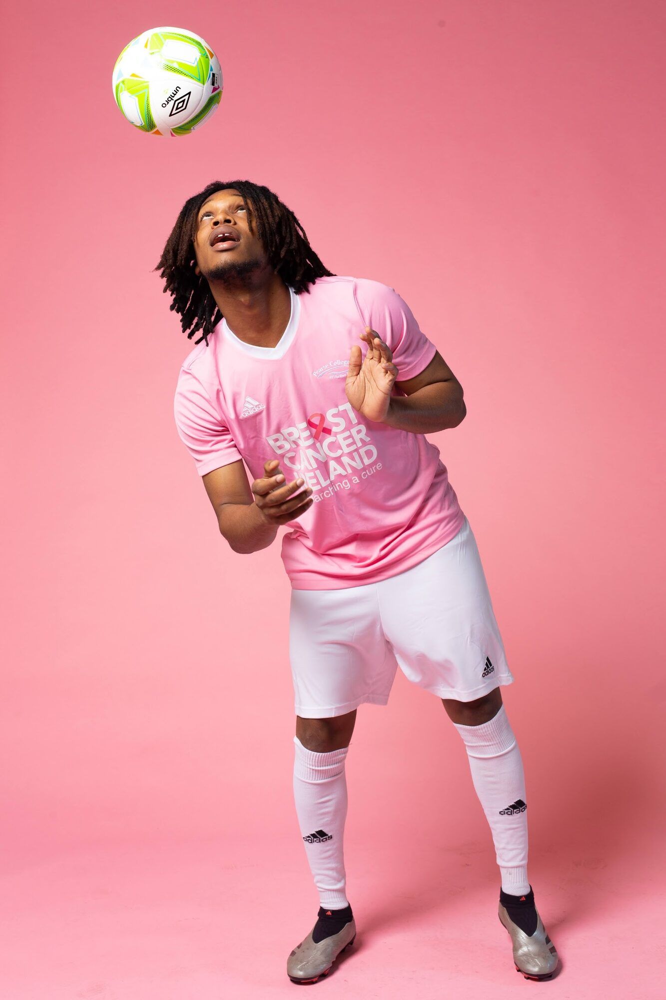 Footballer heading a ball, full length, pink backdrop