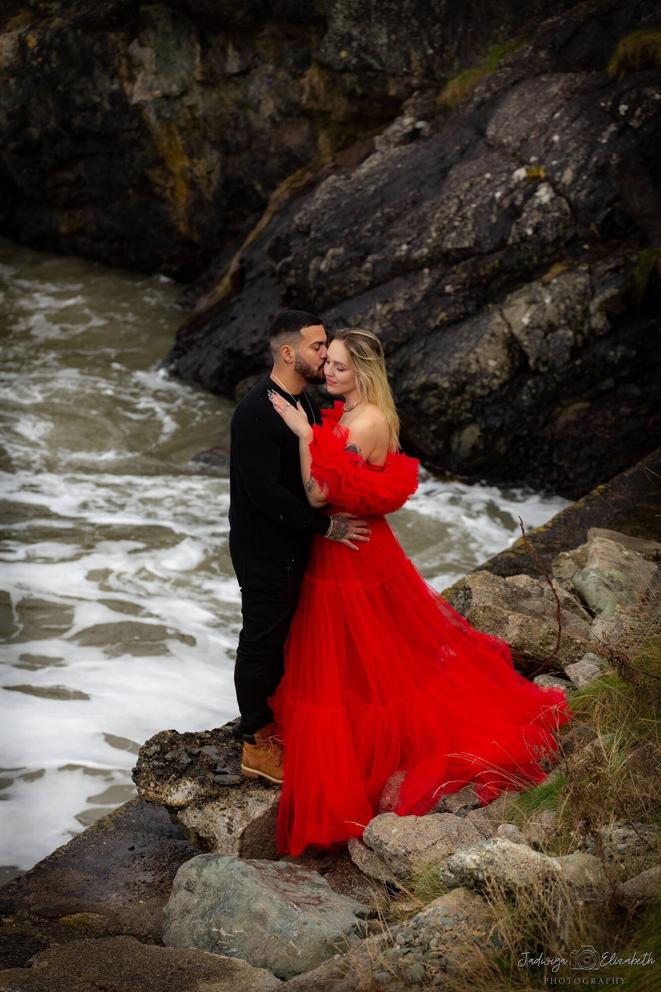 Couple on the rocks, the sea breaking behind