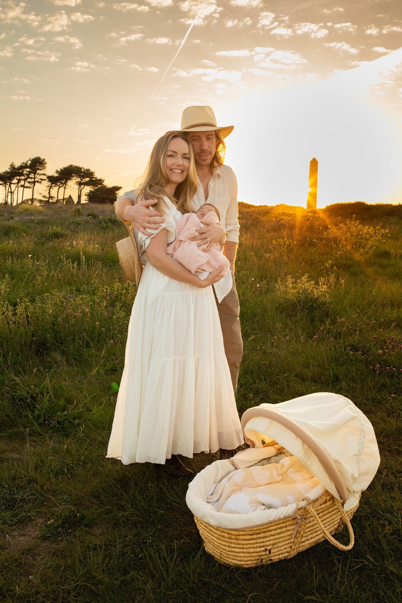 Parents with the baby beside a wicker basket at sunset