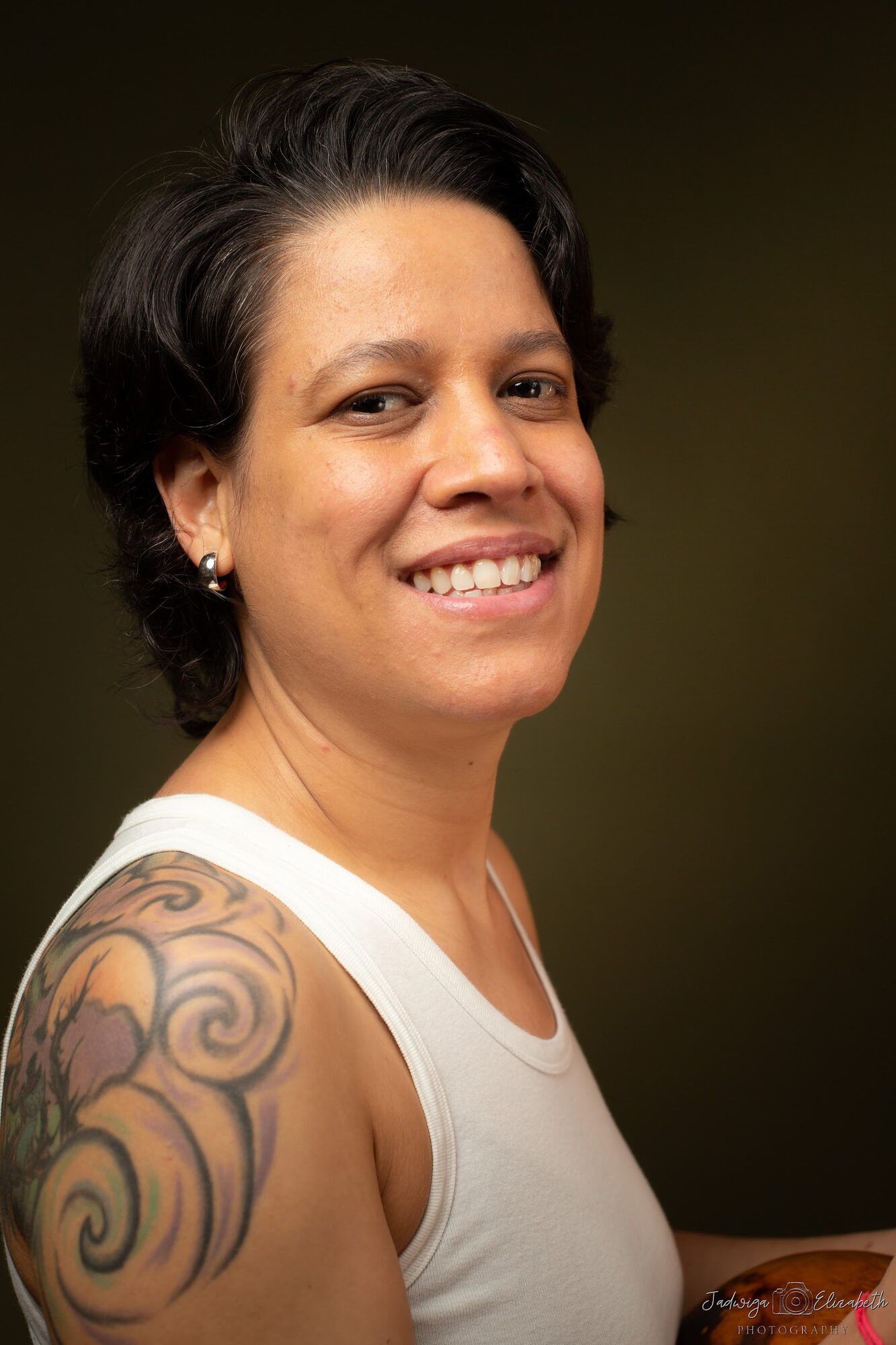 Woman with short dark hair smiling, a tattoo on her shoulder