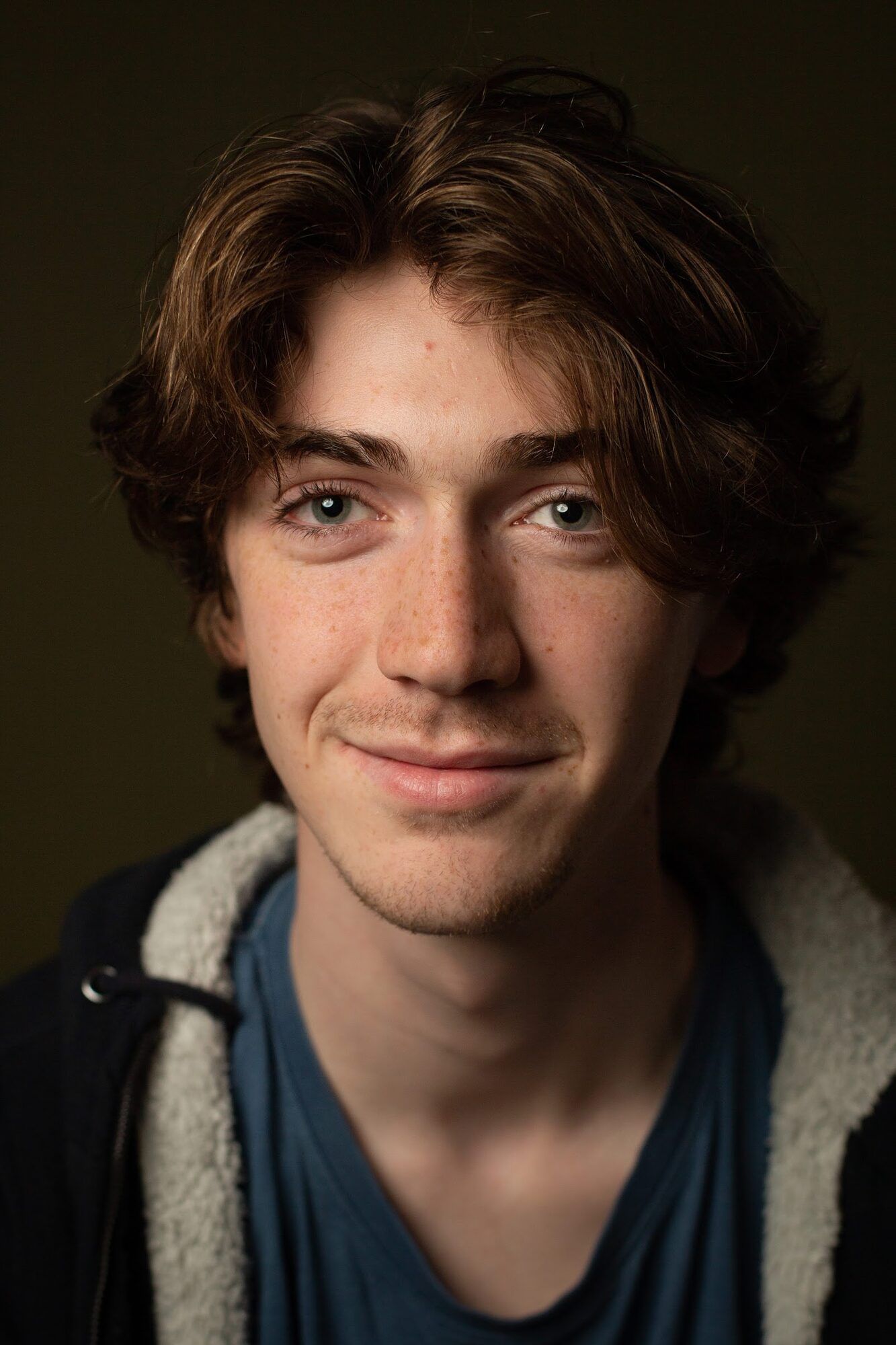 Young man with curly hair, dark backdrop