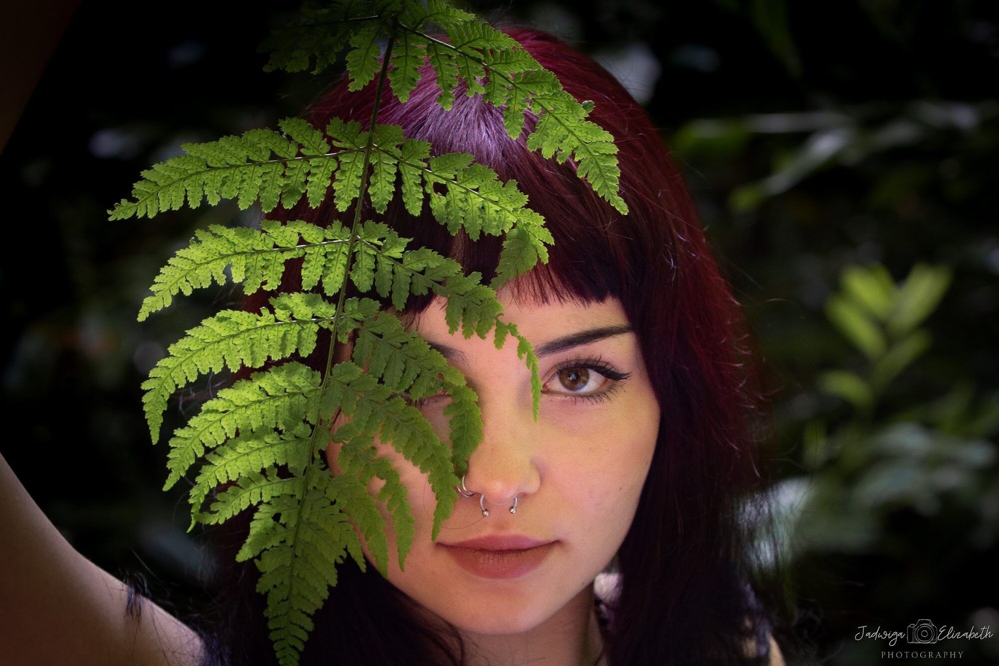 A fern across a dark-haired woman’s face