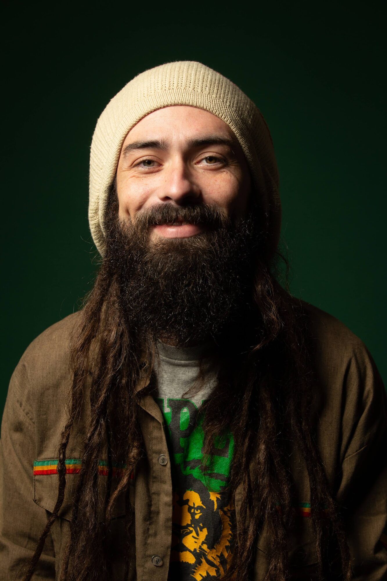 Smiling man with a long beard and a beanie, green backdrop