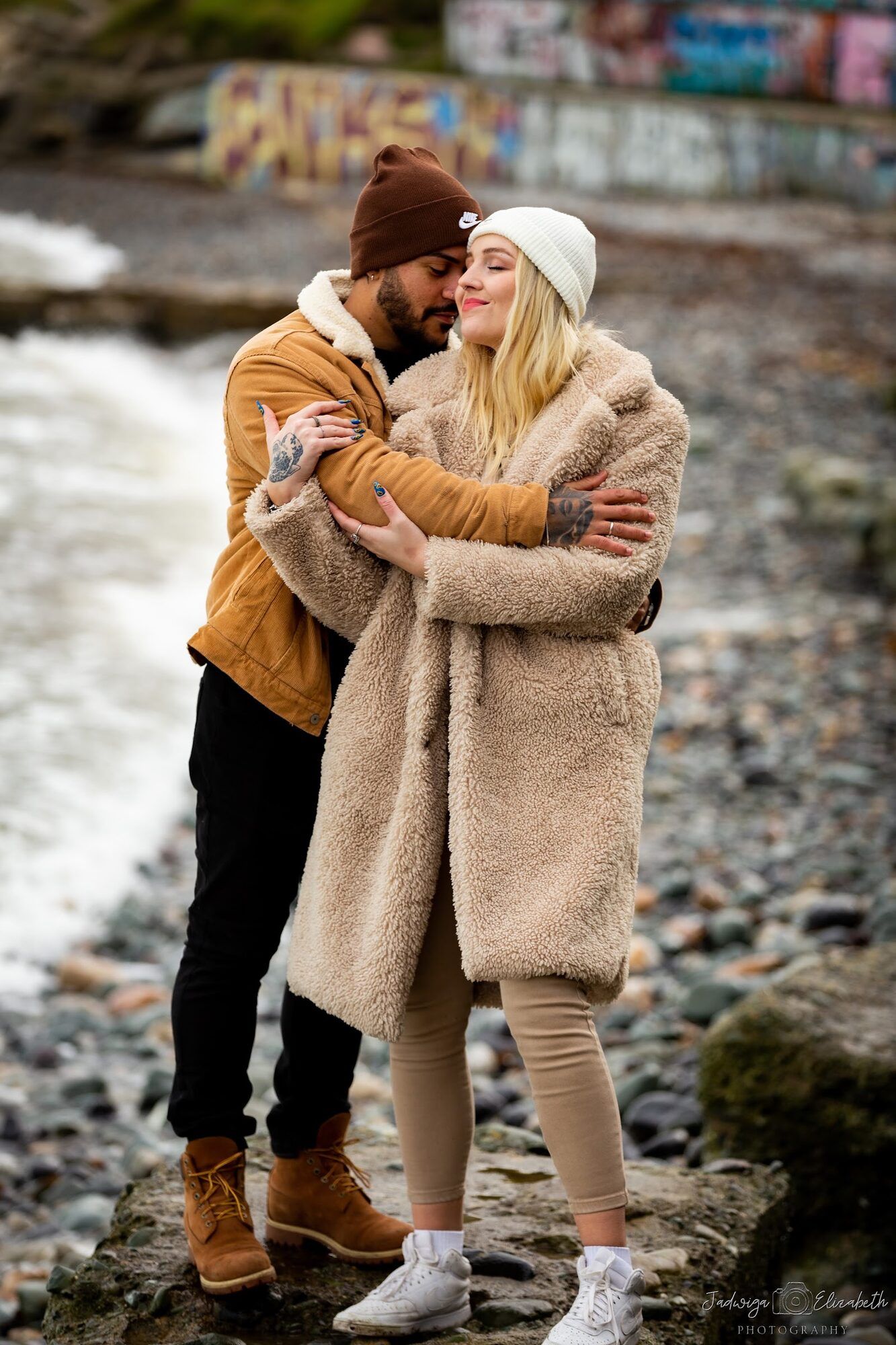 Couple in winter coats hugging on a pebble beach