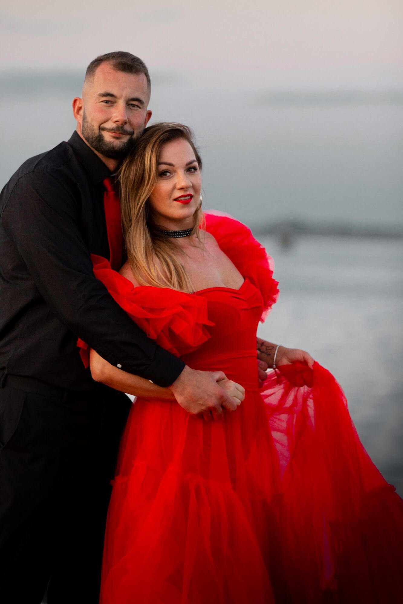 Couple smiling, red gown, the sea behind
