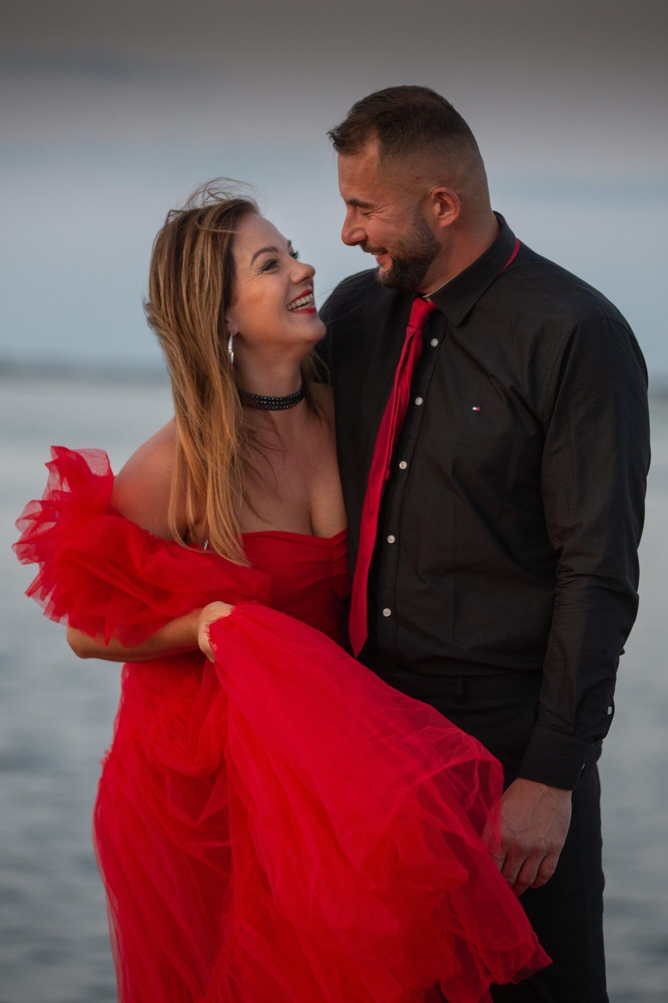 She laughs, lifting the red gown, he in a black shirt