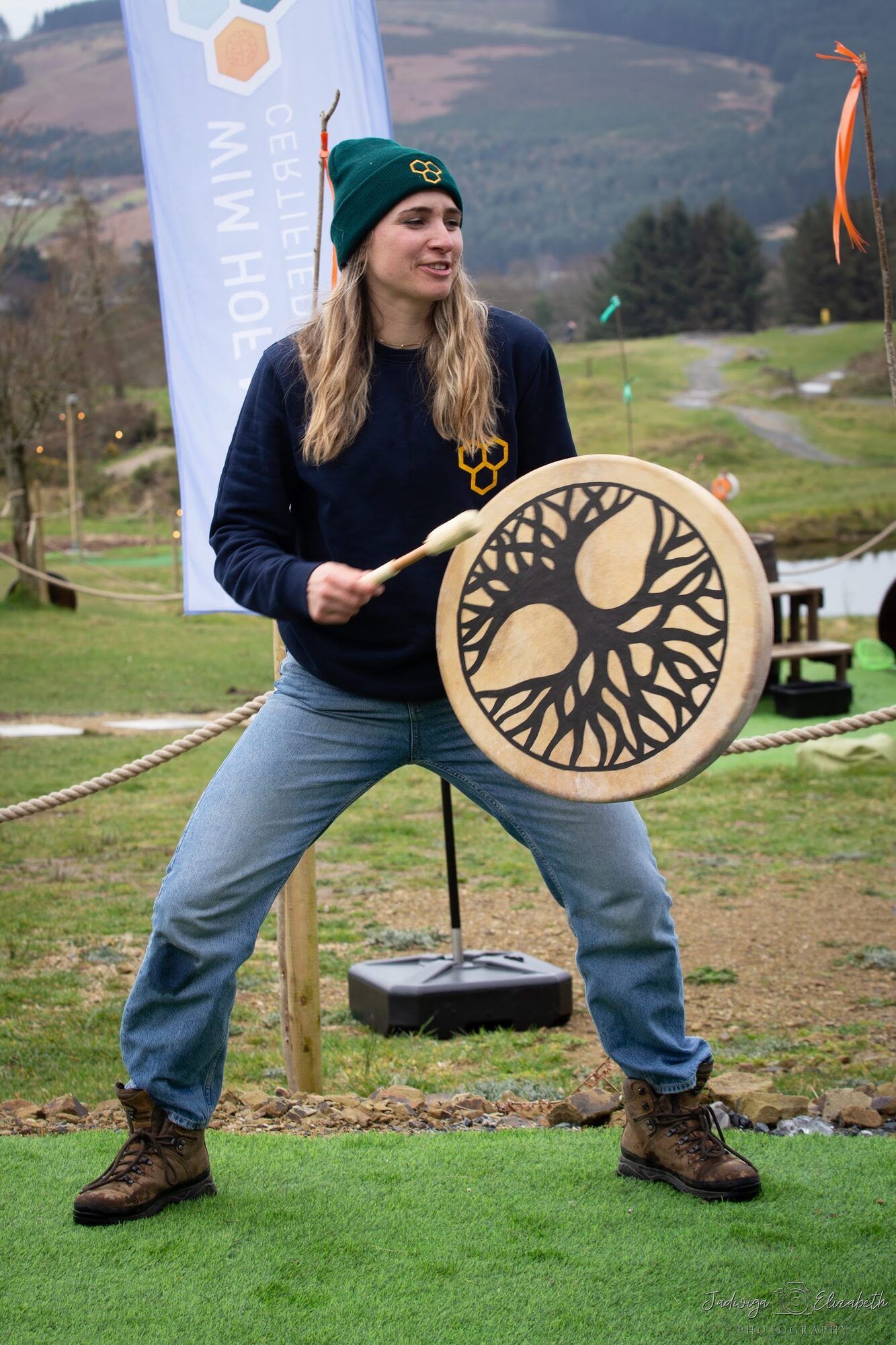 Woman in a green beanie playing a frame drum outdoors