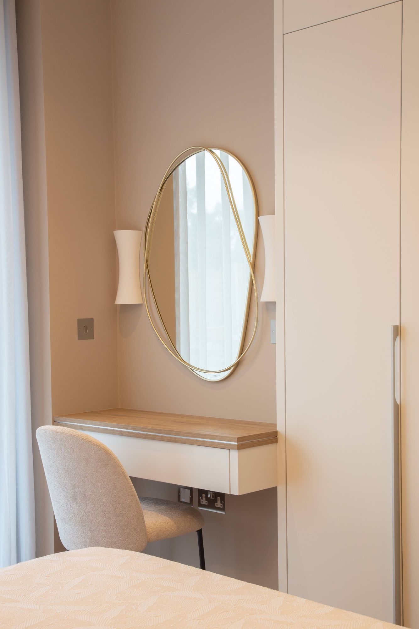 Bedroom dressing table with an oval gold-framed mirror between two wall lights, beside a tall wardrobe